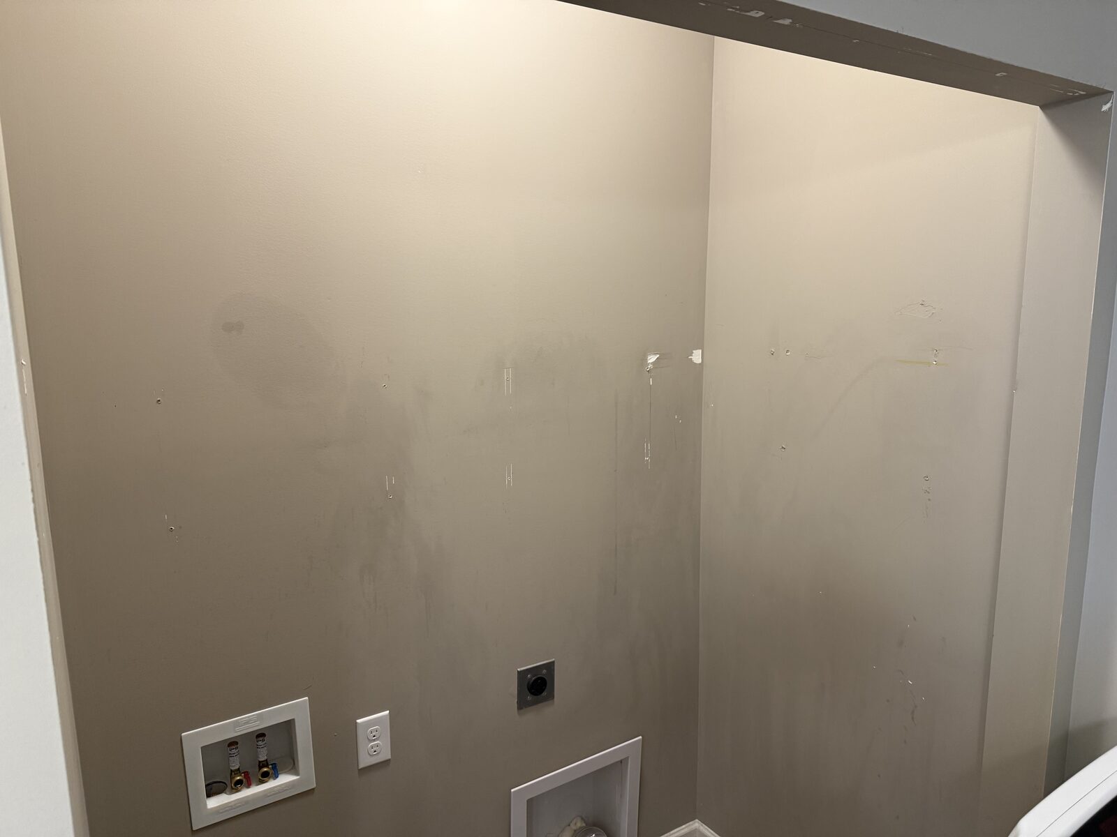 Laundry room wall with shelving removed and visible wall damage before repair